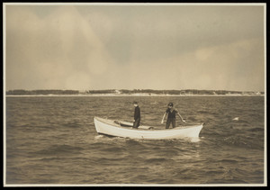 Two boys in a small ship-lapped boat motoring along in front of a beach.