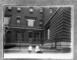 Three children sitting next to a fence in front of Boston Relief Station, Boston, Mass.