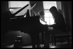 Judy Collins silhouetted against a window, playing piano in her New York apartment