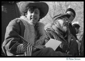 Arlo Guthrie (left, with American flag and sheet of paper with Toshi Seeger's letterhead) and Pete Seeger (partially obscured) seated at an antiwar protest
