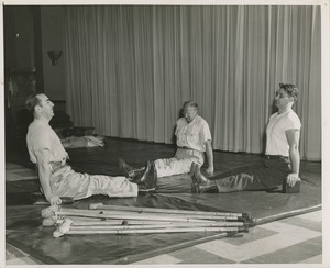 Three men wearing leg braces doing exercises on a gym mat