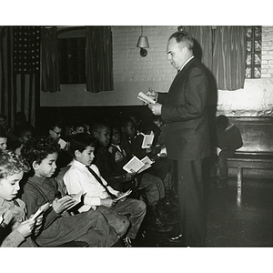 A man directs boys in a sing-a-long from a song booklet