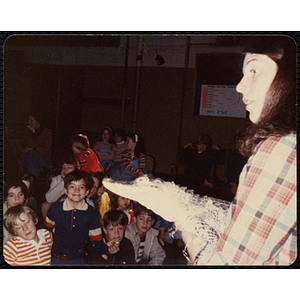 A woman holding an alligator [?] while children look on during the Animal Show