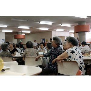 Men and women sit at tables listening to various speakers at a Chinese Resident Association celebration