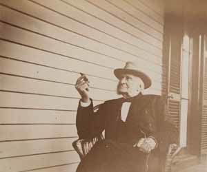 Sidney Bartlett seated in chair on porch, facing left, with cigar