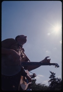 Pete Seeger performing for the crowd at an anti-Vietnam War demonstration: silhouetted against the sky