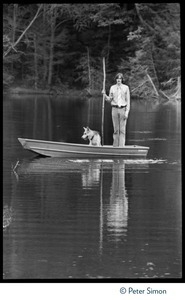 James Taylor standing in a row boat in a pond at Tree Frog Farm commune, with stick and dog