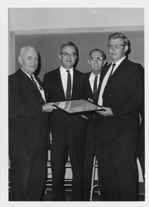 John W. Lederle holding a framed item with three unidentified men