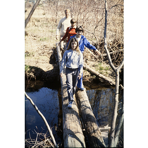 Family walking on logs to cross a creek