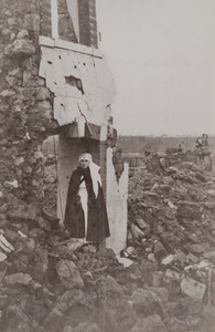 A Red Cross worker standing beneath a destroyed building, the ground strewn with rubble