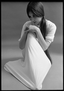 Studio portrait of a model in a loose-fitting shift, seated on the floor, resting her chin on her knee