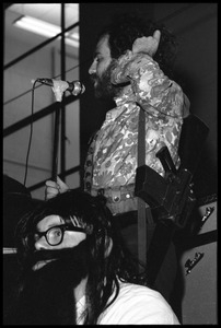 Jerry Rubin, with bandolier and toy assault rifle slung over his shoulder, addressing the audience at the microphone