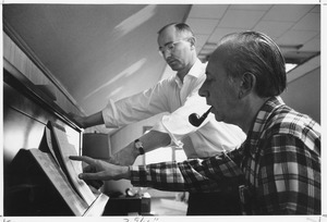 Joseph Langland standing indoors, working with man at piano