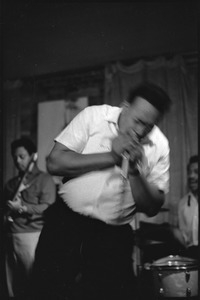 James Cotton at Club 47: James Cotton in motion as he plays harmonica into a microphone onstage, with Luther Tucker playing guitar at left, and Francis Clay playing drums at right