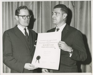 Two men hold the 1960 Thumbs Up Award presented to the Sterling Optical Company