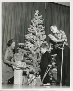 Unidentified woman with man and young boy on crutches in front of Christmas tree