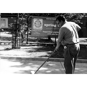 Man with push broom sweeps up a neighborhood park.