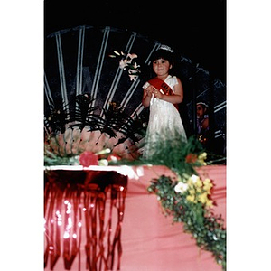 Very young beauty contestant on stage holding a spray of flowers.