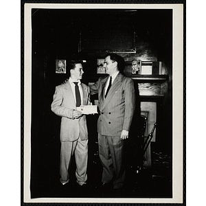 A man presents a check and puts his arm around a young man's shoulder in front of a fireplace at a Boys' Club awards event