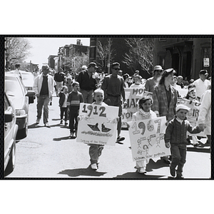 Children and adults marching down the street with signs and banners during the Boys and Girls Clubs of Boston 100th Anniversary Celebration Parade