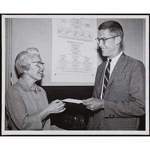Borad of Directors member David B. Stone accpets an envelope from a member of the Mothers' Club in front of a Boys' Clubs organizational flow chart