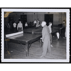 A man plays table tennis with boys in a hall