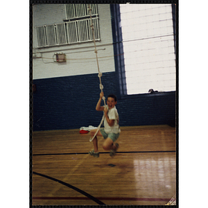 A boy swings on a climbing rope in a gymnasium