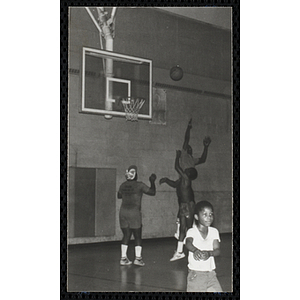 Men and a boy play basketball on indoor court