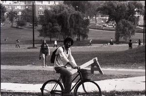 Unidentified man riding bicycle on UMass Amherst campus: Campus Pond and Morrill Hall in background