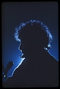 Bob Dylan performing on stage, silhouetted in blue