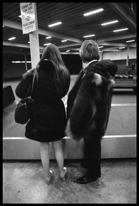 Stephen Stills (in heavy fur coat) and Judy Collins waiting by an airport baggage carousel