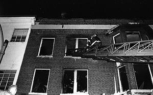 Unidentified firefighter on a ladder in front of a fire-damaged building