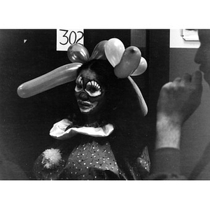 Woman dressed as a clown, with balloons in her hair, stands outside of room 302 at La Alianza Hispana, waiting to entertain the children at the Three Kings' Day celebration