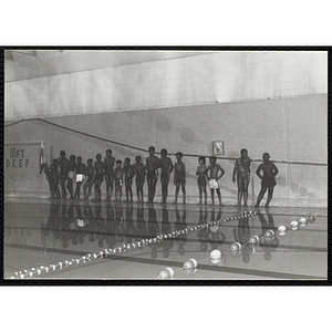 A group of boys stand along a poolside wall in a natorium