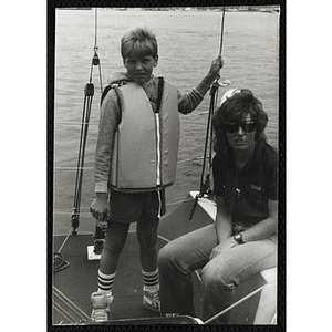 A boy stands next to a woman on the deck of a sailboat in Boston Harbor