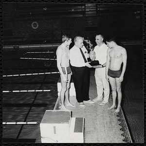 A man presents a trophy to a swimming coach [?] while two swimmers look on at a Boys' Club swimming championship