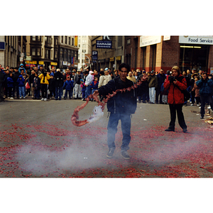 Crowd observes a man performing with firecrackers in the street during a celebration of the Chinese New Year in Boston's Chinatown