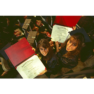 Two students displaying their diplomas at commencement