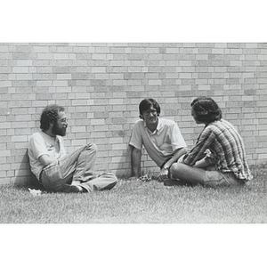 Three men seated on the grass outside Gryzmish Hall