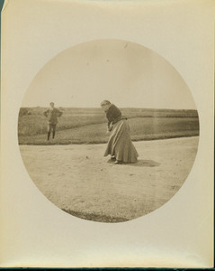 Woman golfer standing in sand trap, in process of swinging club
