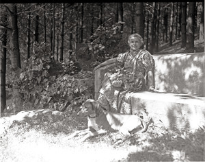 Dorothy Canfield Fisher seated on a bench outdoors, dog at her feet