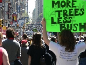 Protester raising a sign 'More trees, less Bush,' marching in the streets to oppose the war in Iraq