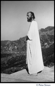 Ram Dass in robes, surveying the landscape from a rock ledge, Lama Foundation