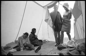 Inside of a strikers' tent, two young women seated on the ground, a couple entering