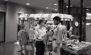 Commune member distributing Free Spirit Press in an indoor shopping mall: communards next to a fruit vendor
