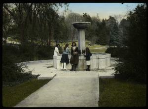 Girls standing by a fountain in a formal garden or park