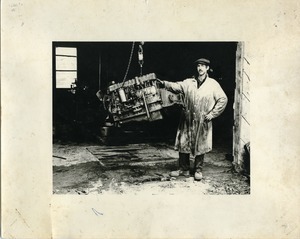 Jim Aaron, posed with a suspended engine block, Montague Farm Commune