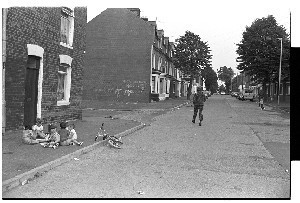 Children playing on Springfield Road, Belfast, unconcerned by the British Army foot patrol walking along the street