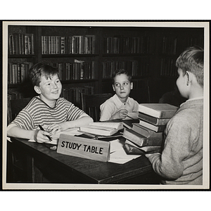 Three boys use a table with a "Study Table" sign on it in a library