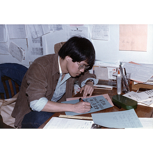 Man seated at a table writes a sign advertising English classes in English and Chinese